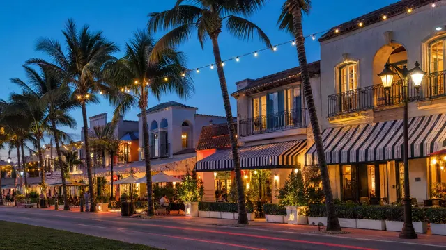A palm-lined main street at dusk, its cafés lit up.
